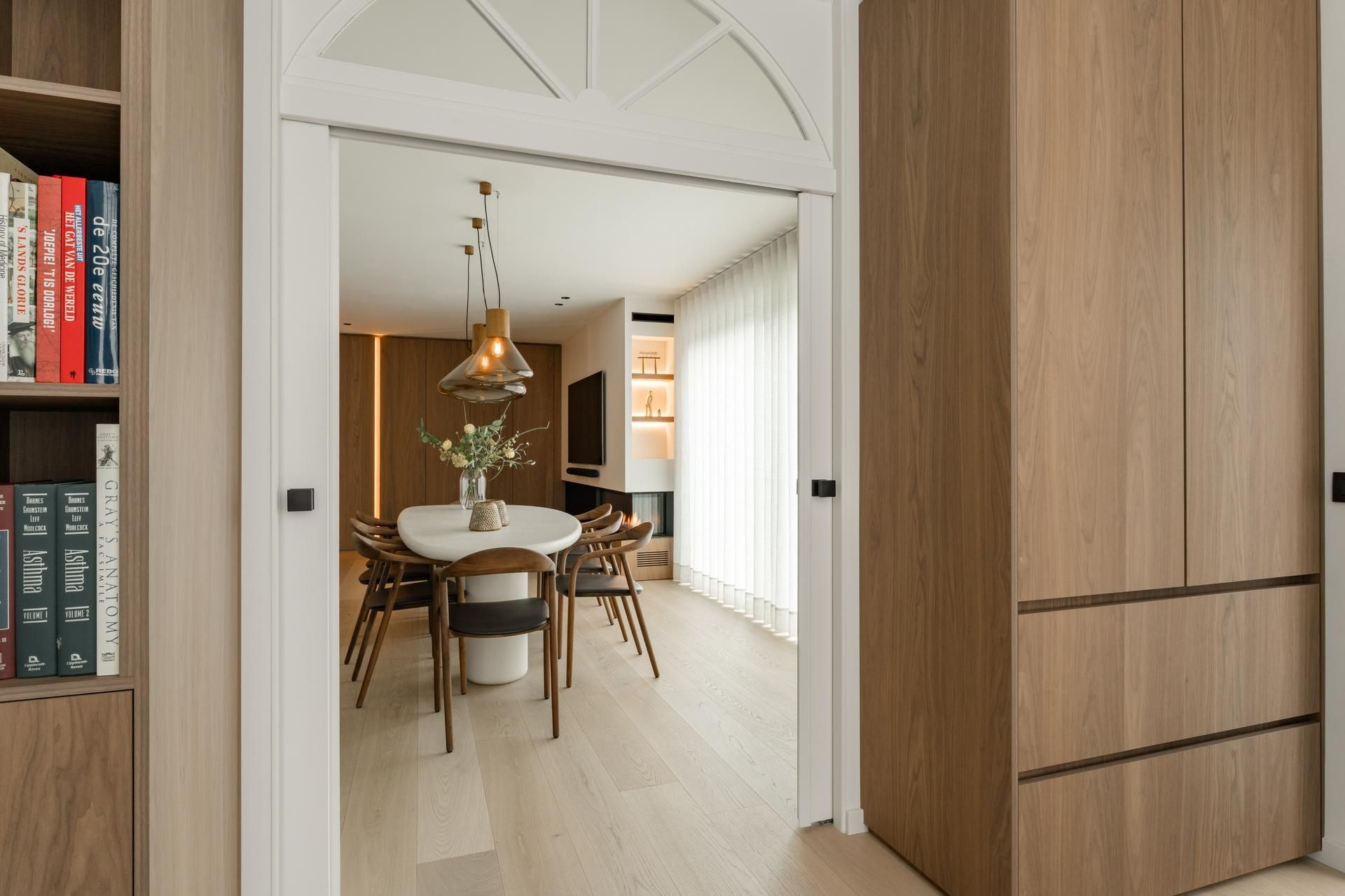 Eetkamer met moderne houten meubels, een ronde tafel en stijlvolle verlichting. Interieurdesign dat esthetiek en comfort verenigt.