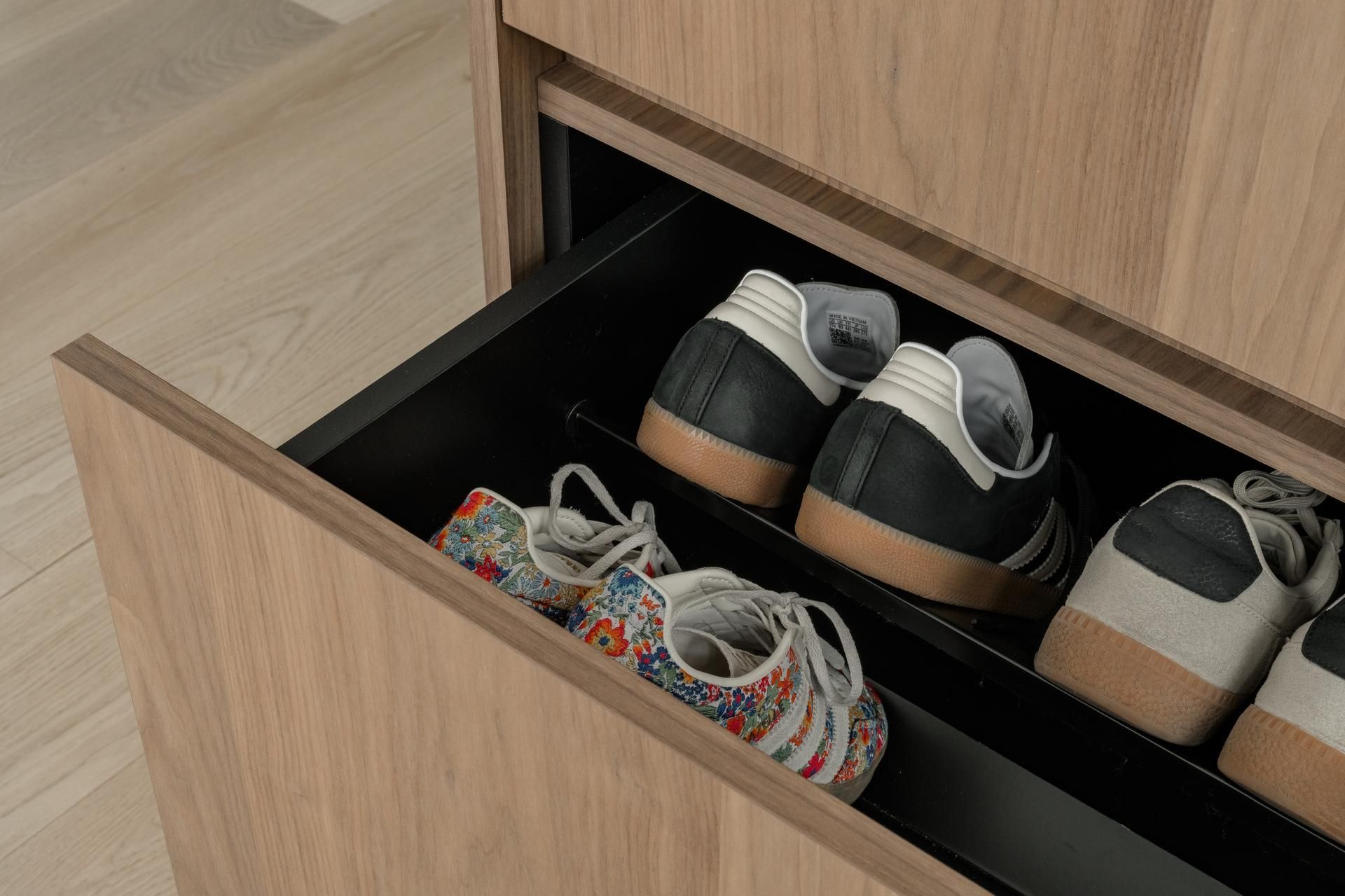 Close-up van een open houten schoenenlade met kleurrijke en zwarte sneakers, passend in een op maat gemaakt interieurontwerp.