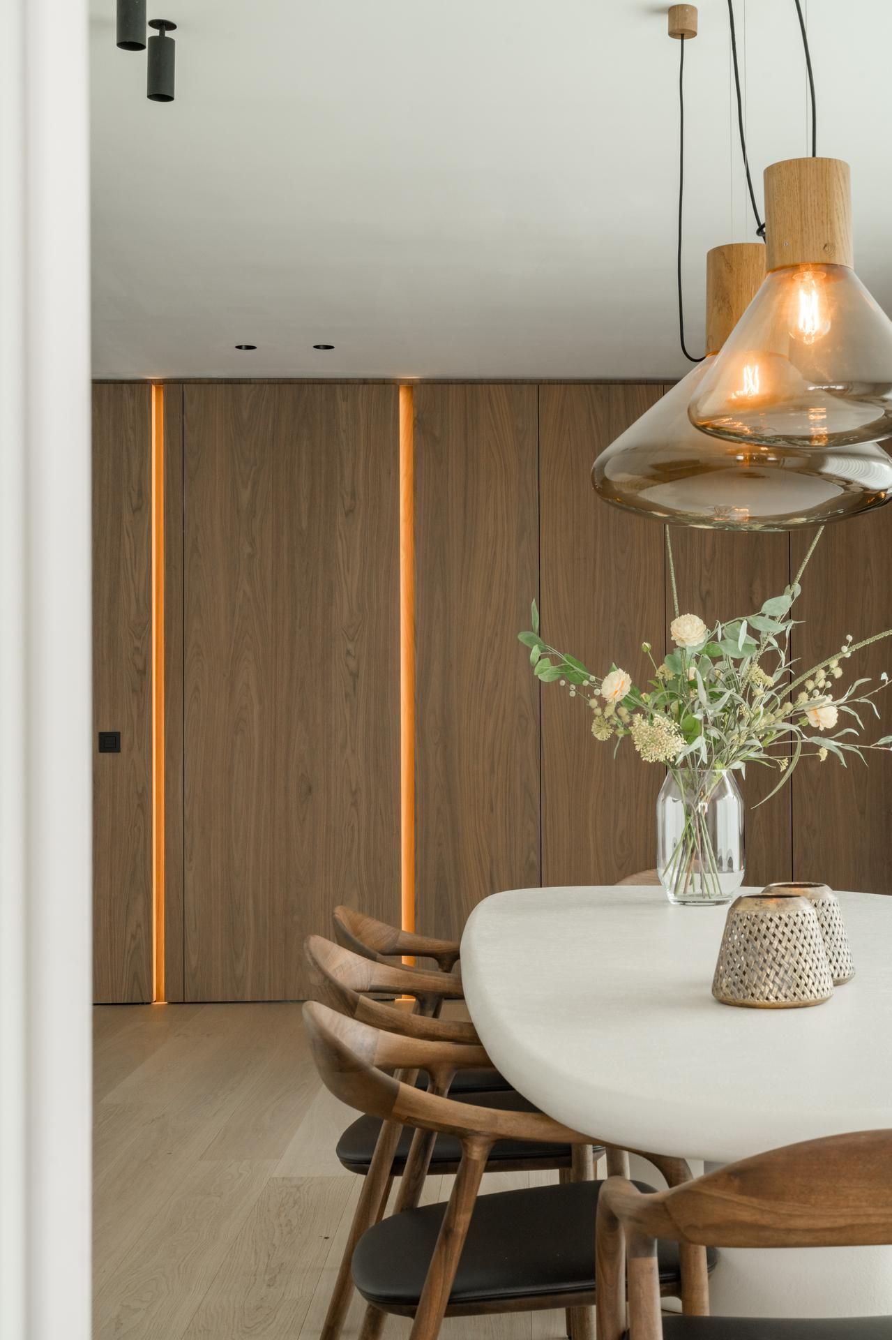 Moderne eetkamerset met houten stoelen en tafel, omgeven door elegante houten kasten en stijlvolle hanglampen.