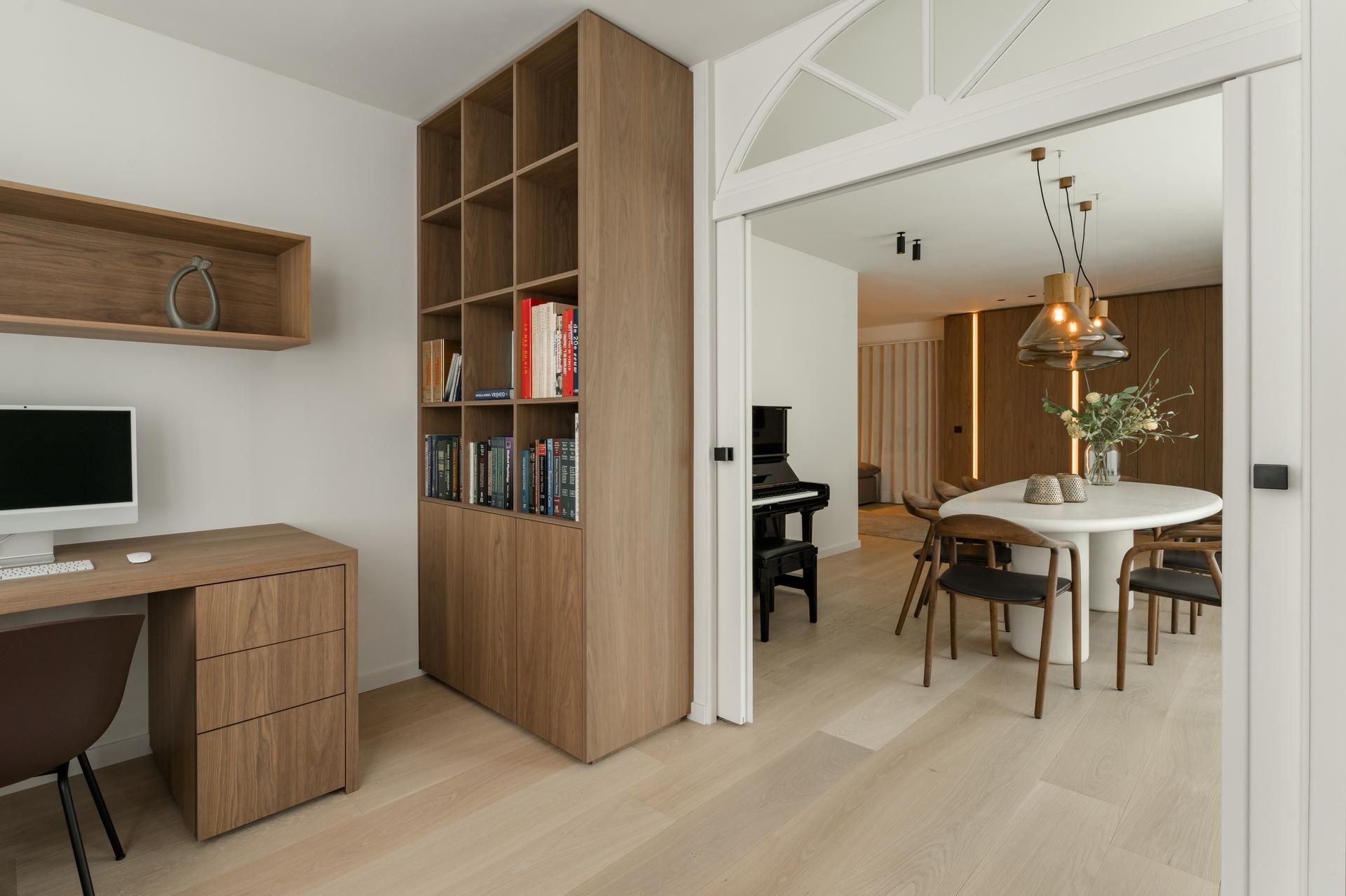 Stijlvol interieur met op maat gemaakte houten kasten, modern bureau en toegang tot een lichte eetkamer met houten meubilair.