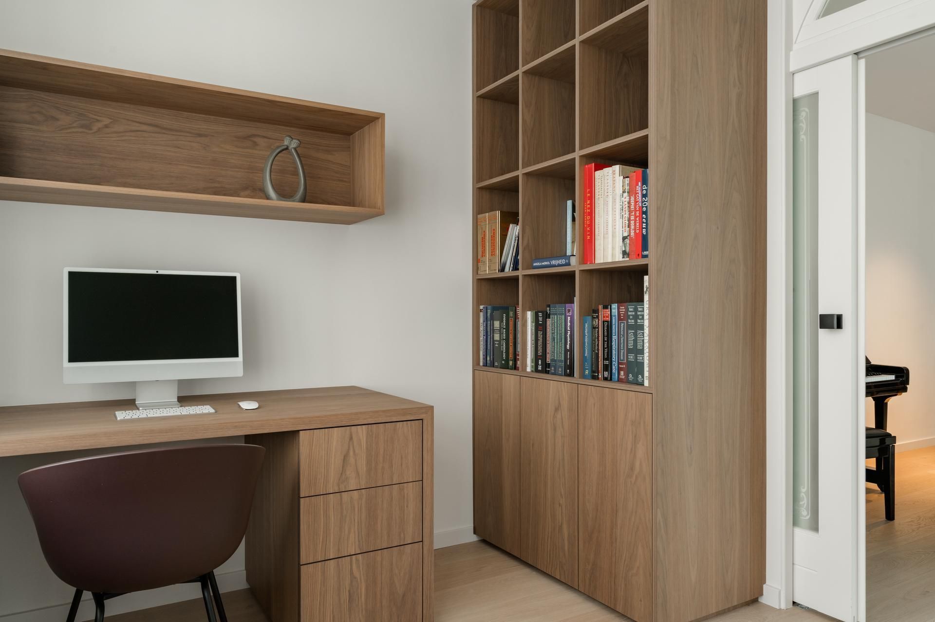 Stijlvolle thuiswerkplek met houten bureau, geïntegreerde boekenplank en moderne computer voor optimaal comfort en functionaliteit.